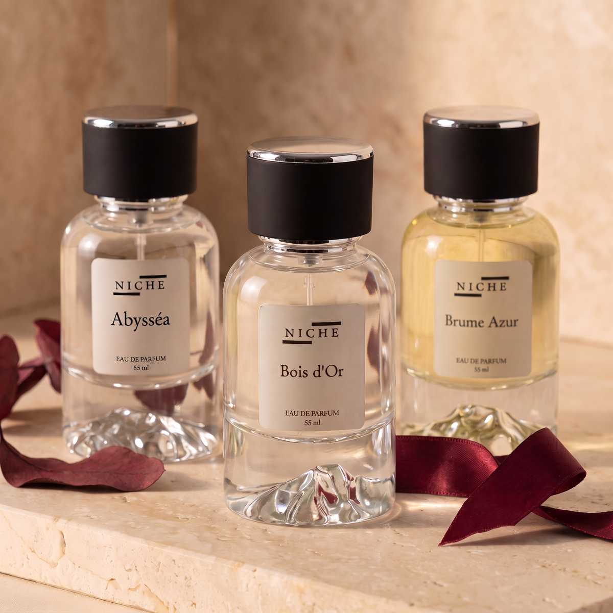 Three Niche Essences perfume bottles—Abysséa, Bois d'Or and Brume Azur—on warm stone